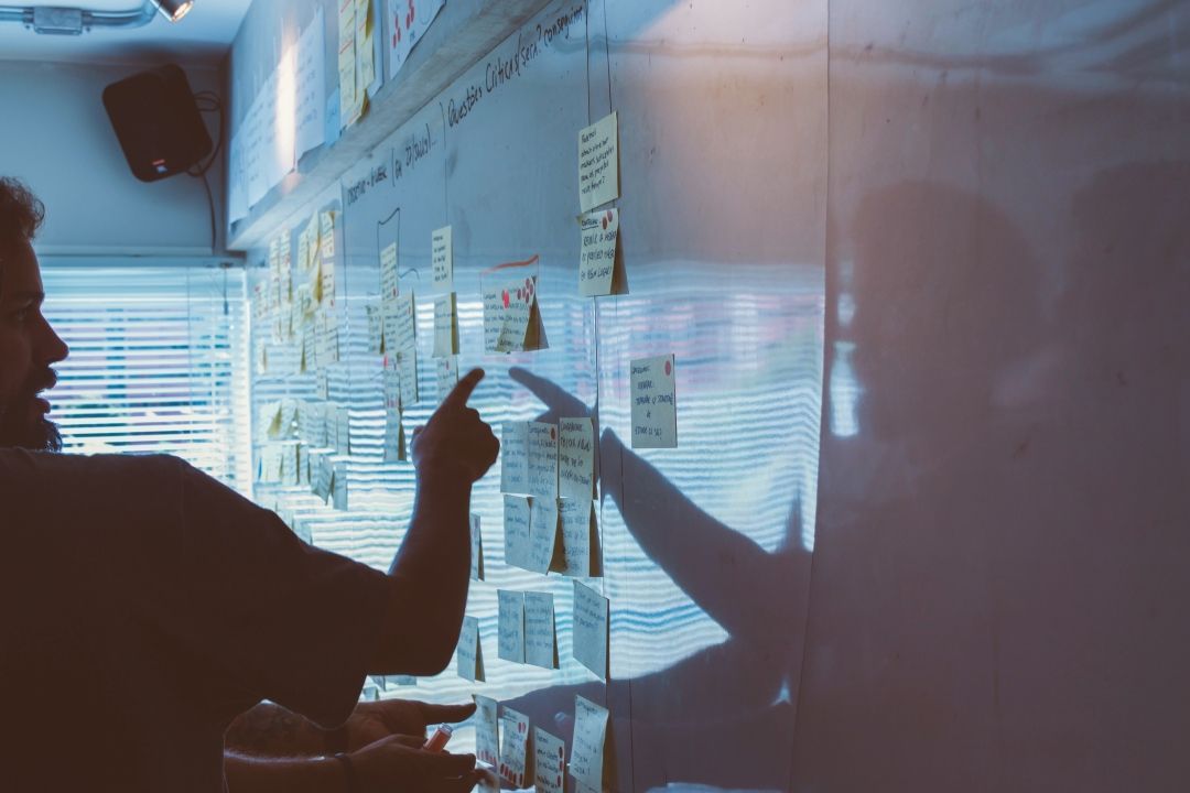 Mann zeigt auf Post-its an Whiteboard