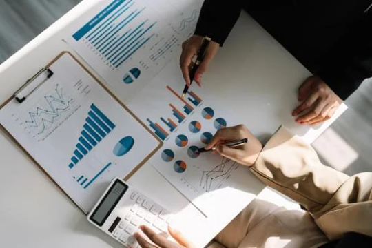Klicken Sie, um das Bild zu bearbeiten 2 Personen sitzen an einem Tisch mit verschiedenen Statistiken und zeigen darauf