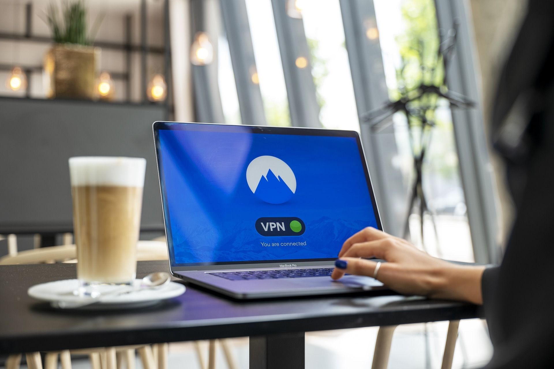 Laptop mit VPN-Verbindung auf dem Screen auf einem Tisch mit Kaffee daneben und einer Frau, die den Laptop bedient