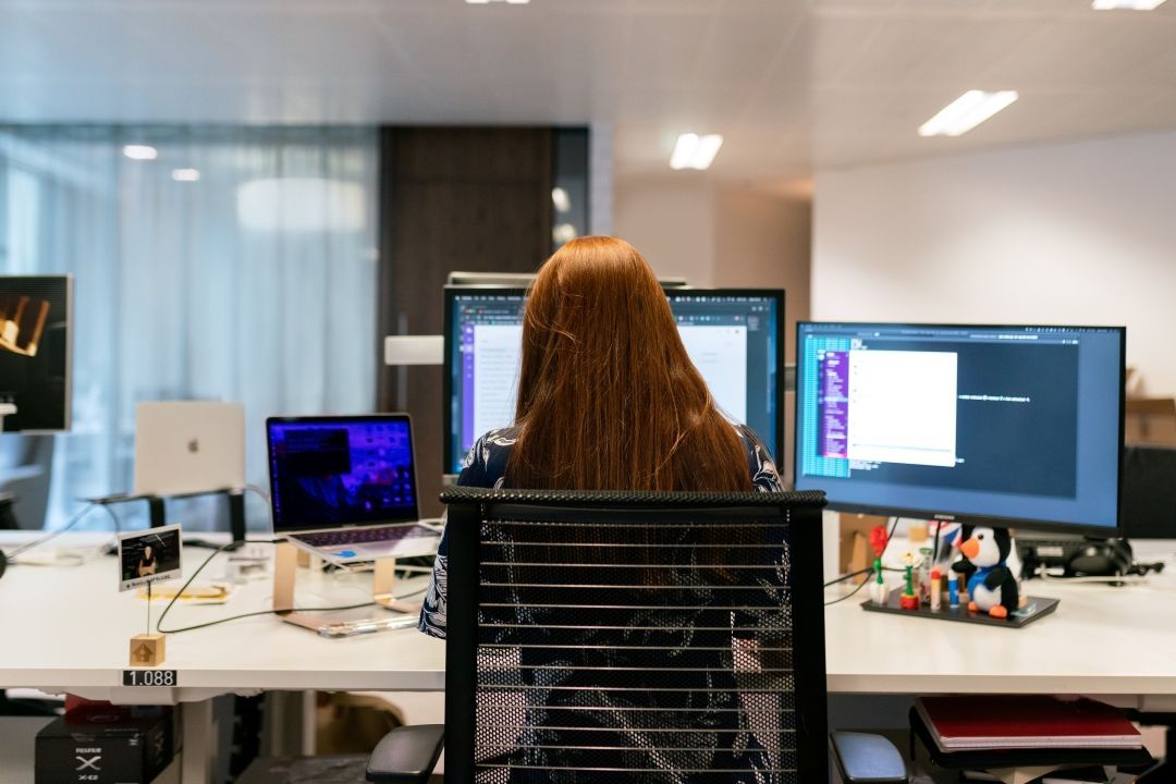 Frau sitzt vor drei Bildschirmen mit einer Unified Communications Lösung