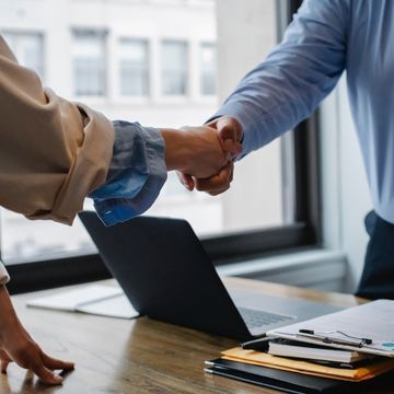 Zwei Personen reichen sich über einen Tisch hinweg die Hand